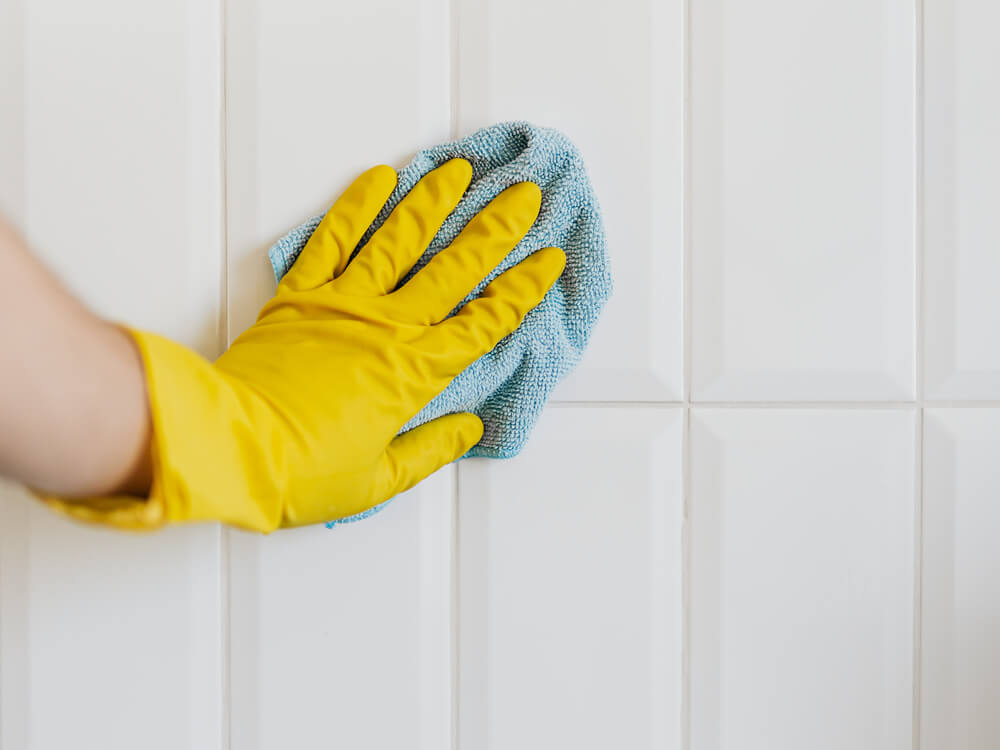 gloved hand cleaning tile and grout